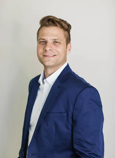 Smiling man in a navy blazer and white shirt against a light gray background