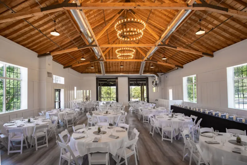 Bright event hall with vaulted wood ceiling, ring chandeliers, and round tables set in white linens