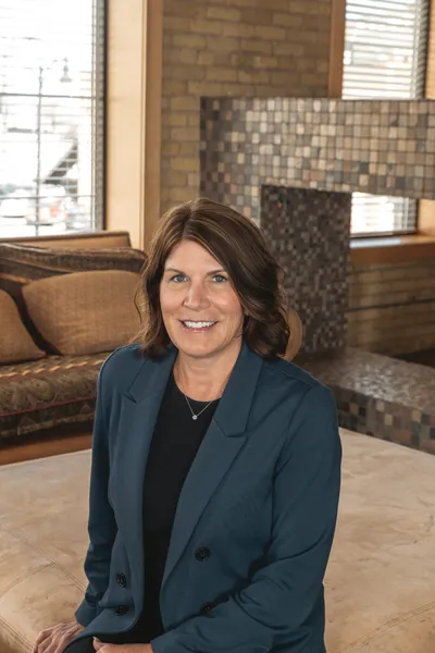 Woman with brown hair in a teal blazer smiling in a warmly lit interior space