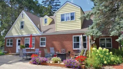 Brick and yellow-sided house with a patio, outdoor furniture, and colorful flower gardens