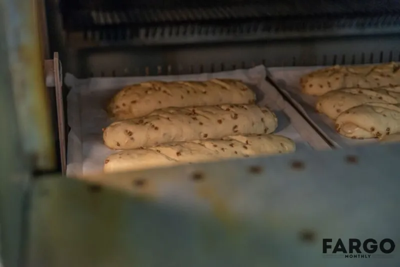 Unbaked seeded bread loaves on parchment-lined trays inside a commercial oven