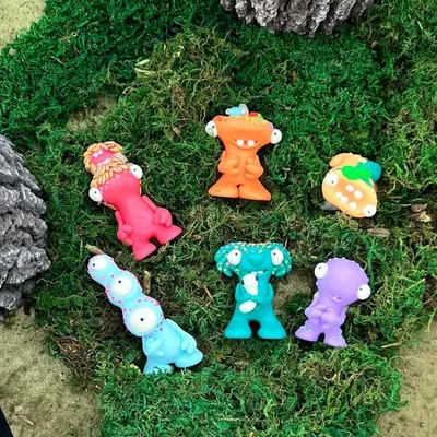 Seven colorful monster-shaped toy figures arranged on green moss