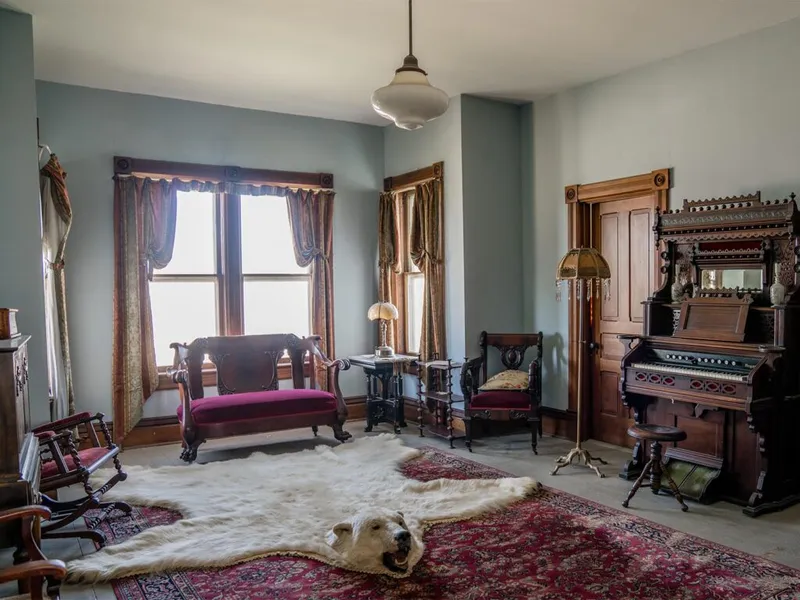 Victorian parlor with ornate pump organ, velvet settee, and white bear-skin rug on patterned floor