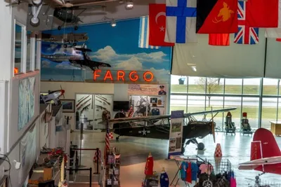 Interior of an aviation museum with vintage aircraft, international flags, and a glowing Fargo sign