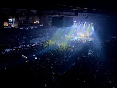 Large indoor arena packed with a crowd facing a brightly lit stage with colorful beams