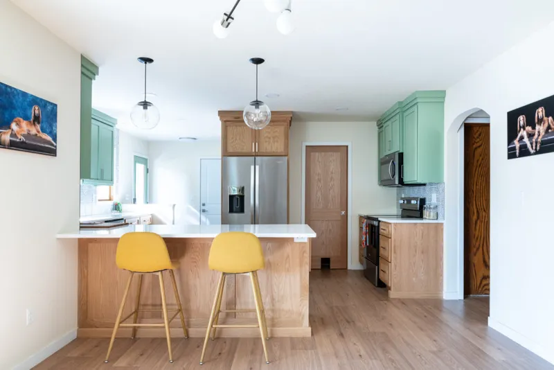 Kitchen with mint green upper cabinets, wood lower cabinets, white island, and two yellow barstools
