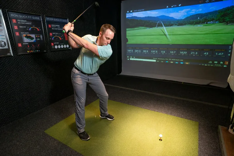 Man mid-swing on an indoor golf simulator mat with shot-data screen behind him