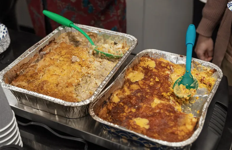 Two partially served casseroles in foil pans with green serving spoons