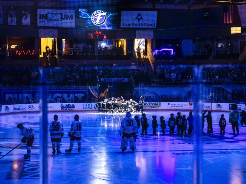 Hockey players on ice under blue arena lights during a pre-game ceremony