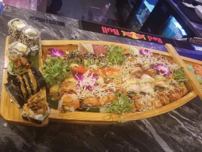 Assorted sushi rolls arranged on a wooden boat platter with greens and purple orchids