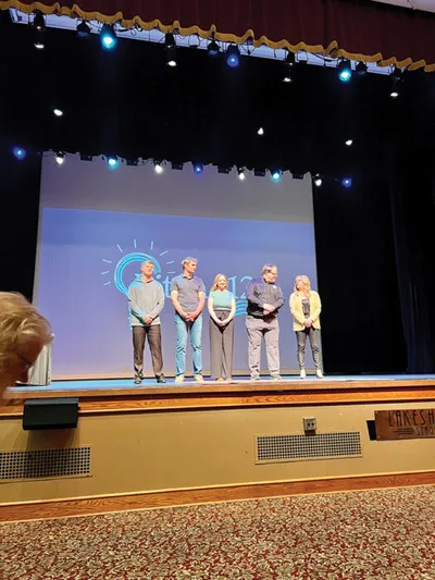 Four people standing on a theater stage in front of a projected logo