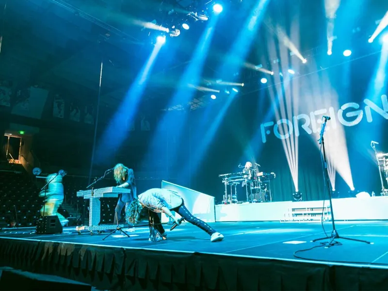 Foreigner band performing on a blue-lit stage, vocalist bent low holding a mic
