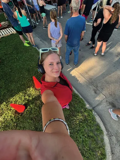 Woman in red top with headphones and sunglasses takes a selfie at an outdoor community event