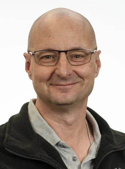 Bald man with glasses smiling in a headshot against a white background