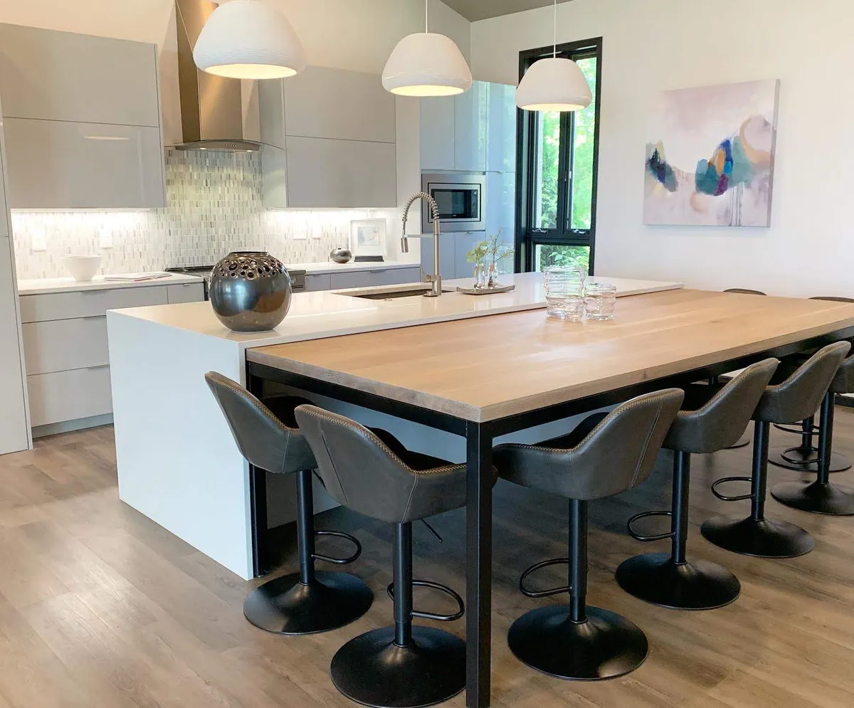 Modern kitchen with a large wood-top island, gray bar stools, pendant lights, and abstract wall art