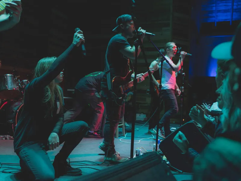 Rock band performs on a dim stage as energetic fans sing and reach toward the performers