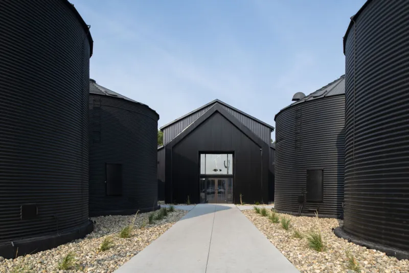 Concrete path flanked by large black corrugated silos leading to a black barn-style building