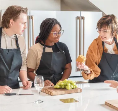 Three people in dark aprons gather around a cutting board with grapes during a cooking class