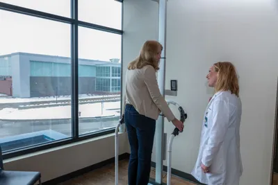 Woman being measured for height by a clinician in a white coat near a large window