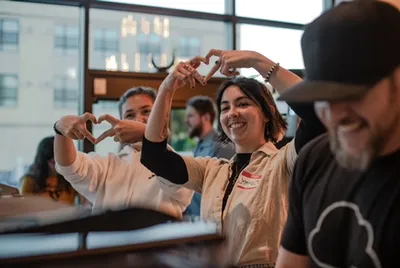 Smiling woman in a café making a heart shape with her hands alongside coworkers