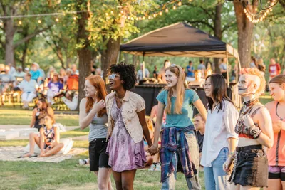 A group of young women laughing and holding hands at an outdoor community festival