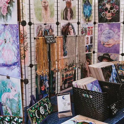 Artist market booth displaying colorful fantasy art prints and dangling chain jewelry on a grid wall