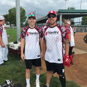 Two softball players in matching Nardini jerseys and caps posing at a baseball complex
