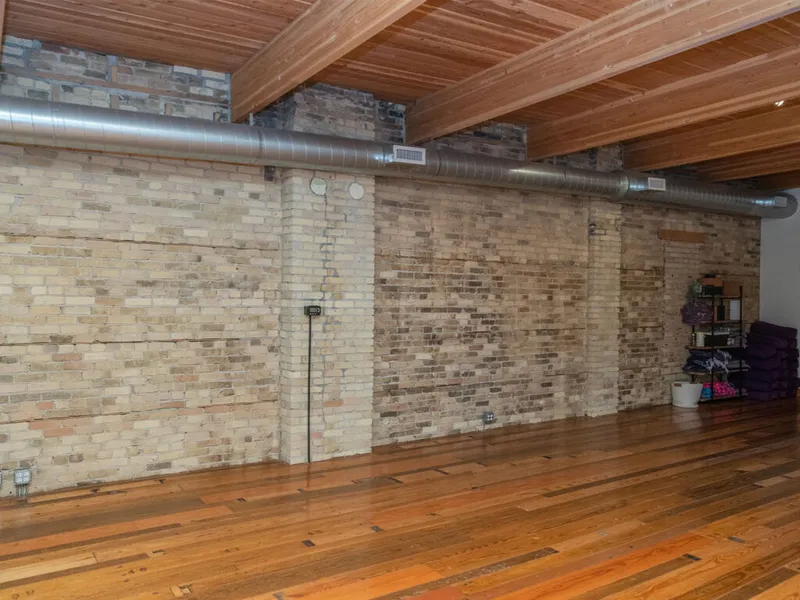 Open loft studio with exposed brick walls, wood-beam ceiling, metal ductwork, and hardwood floors