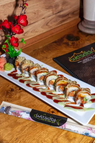 Sushi rolls drizzled with red and green sauce on a white rectangular plate
