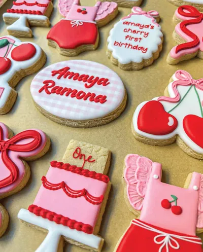 Decorated sugar cookies with cherry and birthday themes, reading "Amaya Ramona" and "One