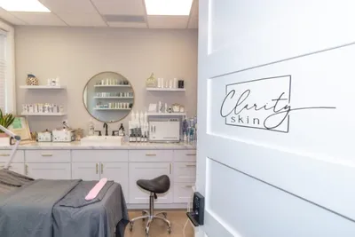 Clarity Skin treatment room with a gray facial bed, round mirror, and product shelves