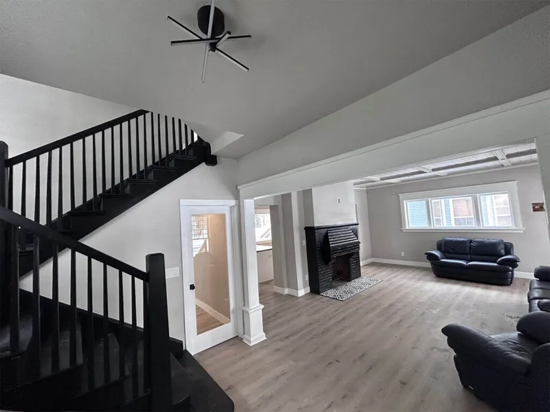 Open living room with black staircase, dark brick fireplace, and navy leather sofas on light wood floors