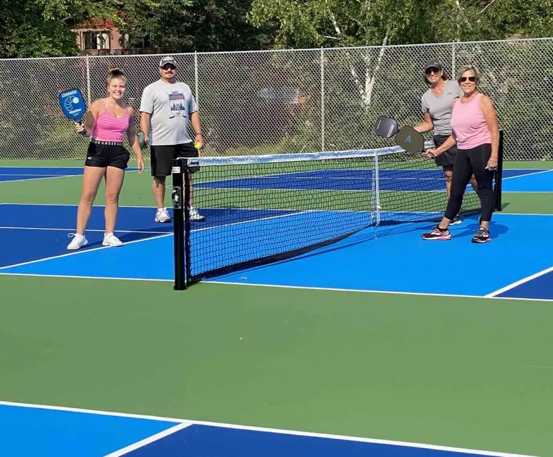 Four players with pickleball paddles posed at the net on a blue and green outdoor court