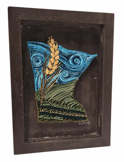 Framed paper quilling art shaped like Minnesota with swirling blue sky and golden wheat stalk