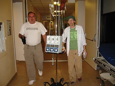Two men walking down a hospital corridor beside an IV drip stand