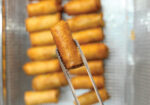 Golden fried tater tots on a skewer held above a tray