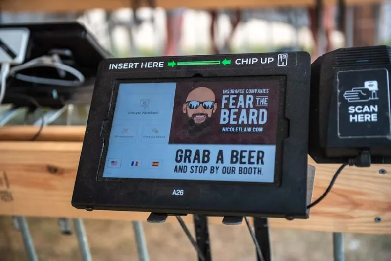 Festival payment kiosk displaying a sponsored ad reading 'Grab a Beer and Stop By Our Booth