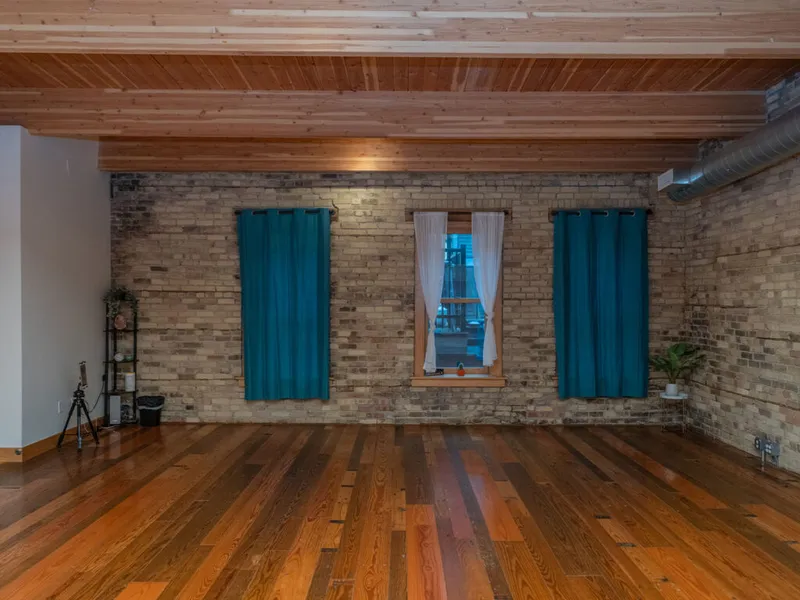 Open yoga studio with polished hardwood floors, exposed brick wall, and teal curtains