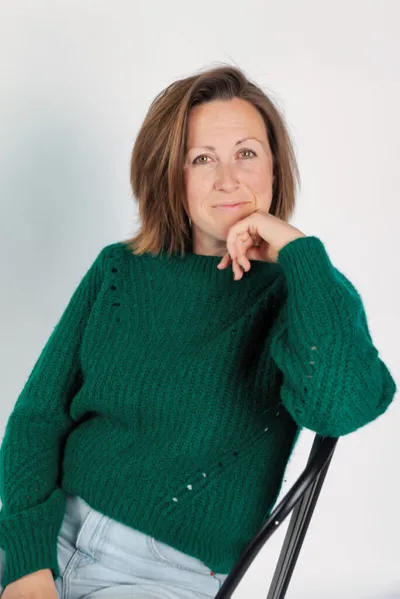 Woman in green knit sweater seated on a chair, resting chin on hand