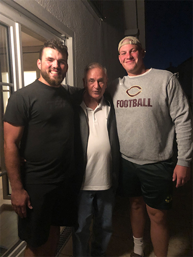 Two large young men flanking an older man, one wearing a Chicago Bears football sweatshirt