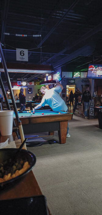 Person leaning over a pool table to take a shot in a dimly lit bar arcade