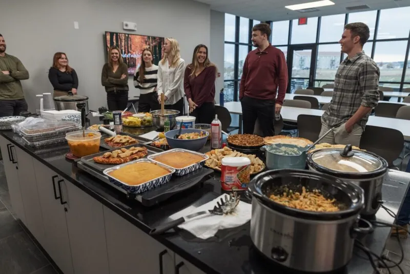 Group of coworkers gathered around a counter spread with potluck dishes and slow cookers