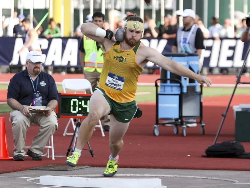 Bearded male athlete in yellow NDSU jersey releases shot put at NCAA track and field competition