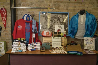 Boutique display table with folded shirts, hats, a blue jacket on mannequin, and a framed vintage photo