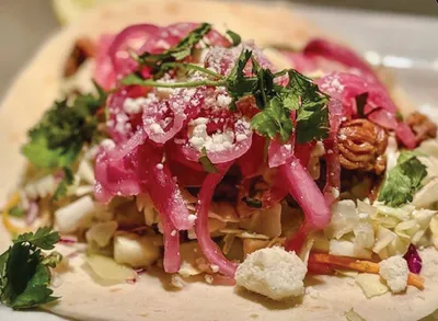 Taco topped with pickled red onions, crumbled white cheese, shredded cabbage, and fresh herbs on a flour tortilla