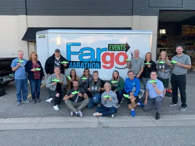 Group of people holding green shoes in front of a Fargo Marathon Events trailer