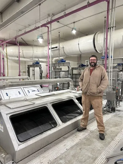 Bearded man in work clothes standing beside large industrial equipment in a utility facility