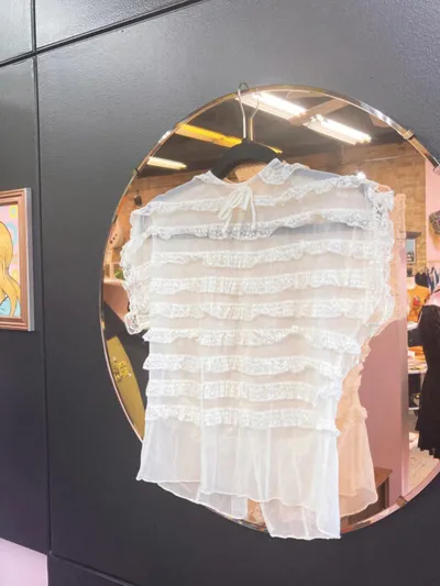 White ruffled lace blouse on a hanger reflected in a round gold-framed mirror