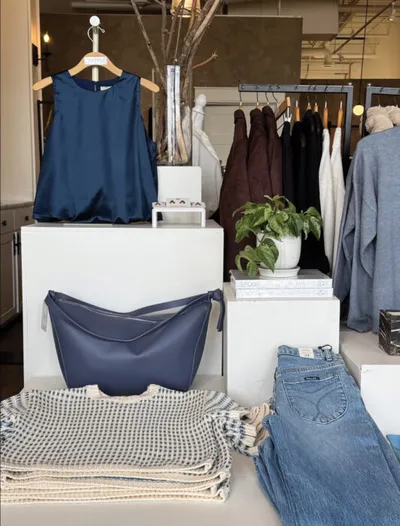 Boutique display with navy sleeveless top, leather bag, folded jeans, and a clothing rack