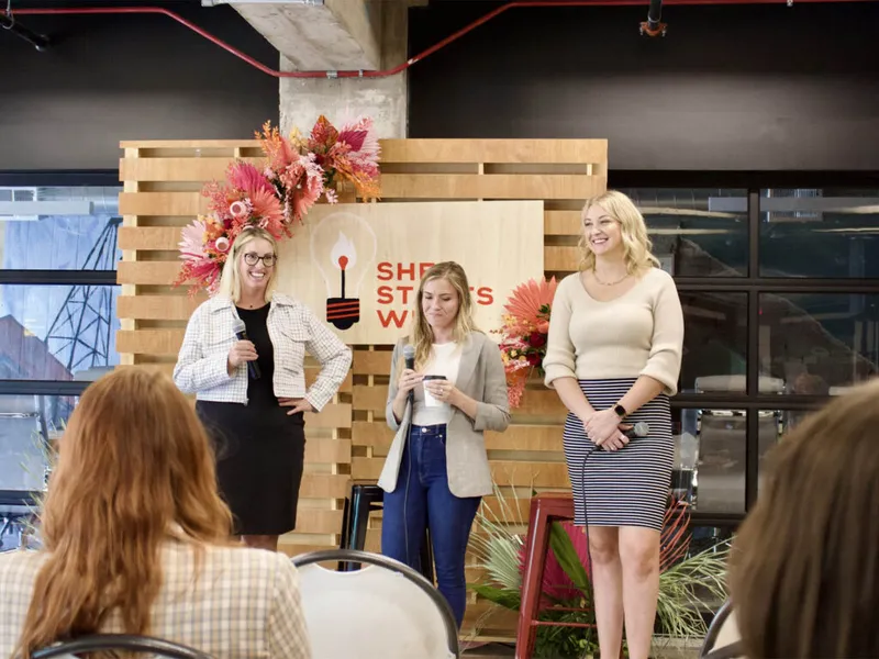 Three women speaking on stage before an audience at an indoor panel event